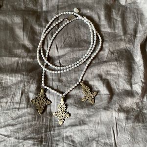 Silver pearl like beads with 3 crosses. Can be worn long or short